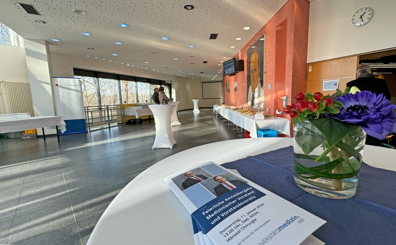 Foyer Hörsaal 505 mit einem dekorierten Stehtisch mit Flyern und Blumen im Vordergrund.